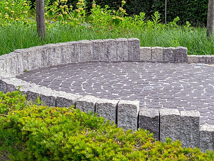 Flagstone patio with a stacked-stone fire pit, cushioned seating and hydrangea beds behind a brick home